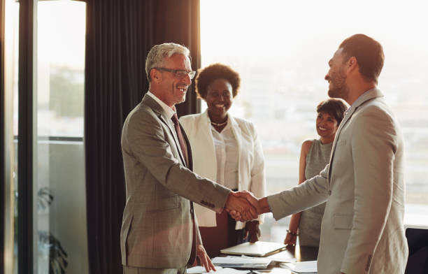 istock Smiling businessmen shaking hands with colleagues in the background 1180329355