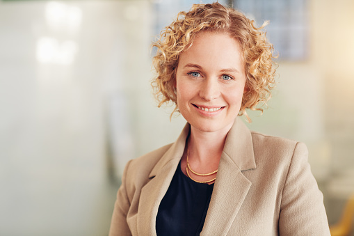 Portrait of a smiling young blonde businesswoman wearing a suit standing alone in a large modern office