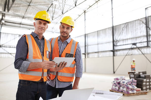 istock Smiling building engineers wearing safety gear using a digital tablet 1180334785