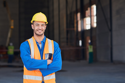 Portrait of a smiling construction engineer in workwear standing with his arms crossed at a warehouse entrance