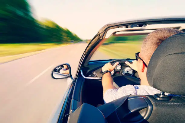 Man driving a convertible car on country road. View from the inside behind the driver. man is driving at high speed on the highway. Dangerous fast driving. Motion blur effect