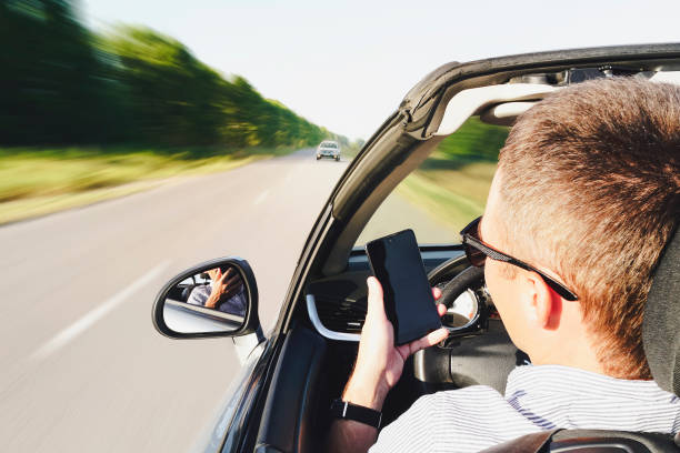 primo piano dell'uomo che usa uno smartphone mentre guida un'auto. guida nel traffico in arrivo. movimento pericoloso. distratto dal telefono. il ragazzo scrive un messaggio al telefono mentre guida. effetto movimento sfocato - driving text messaging accident danger foto e immagini stock