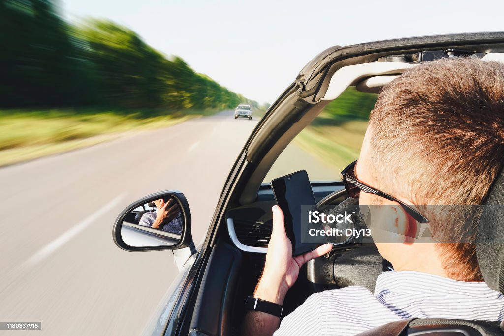 자동차를 운전하는 동안 스마트 폰을 사용하는 남자의 클로즈업. 다가오는 트래픽으로 운전. 위험한 움직임. 전화로 산만. 남자는 운전하는 동안 전화로 메시지를 씁니다. 효과 흐린 모션 - 로열티 프리 부주의한 스톡 사진