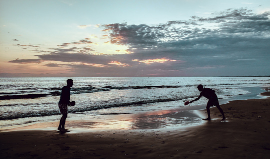 an homosexual couple playing paddle in the beach over a beautiful sunset