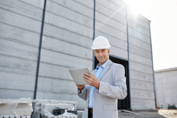 ingénieur mûr de sourire utilisant sa tablette numérique sur un chantier - building contractor flash photos et images de collection