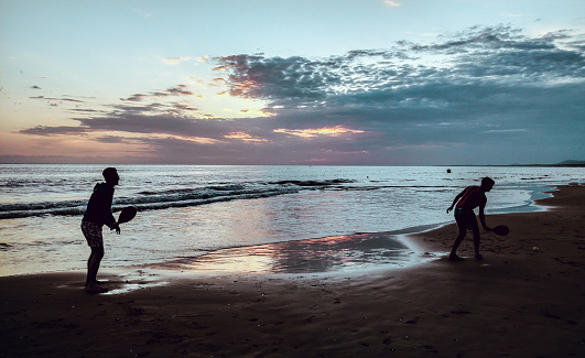 an homosexual couple playing paddle in the beach over a beautiful sunset