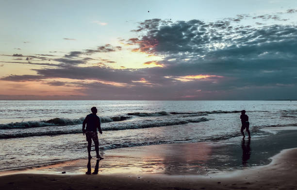 A setting sun over the sea and walkers on the beach, Westward Ho! North Devon