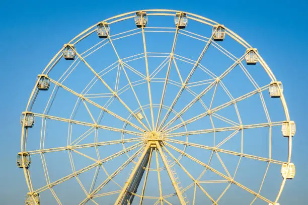 image of a white ferris wheel against blue sky. Cabins of the Ferris wheel.