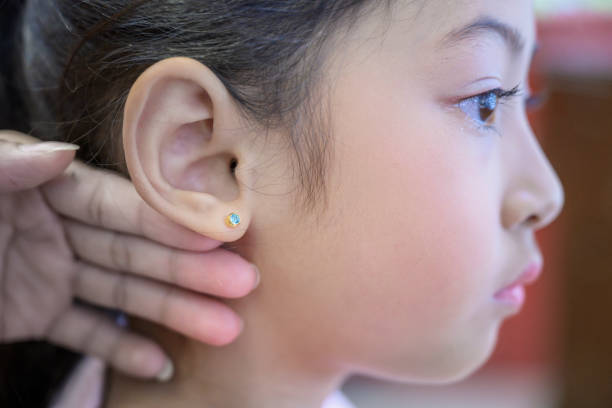 istock Adorable little asian girl having ear piercing process. 1180343424