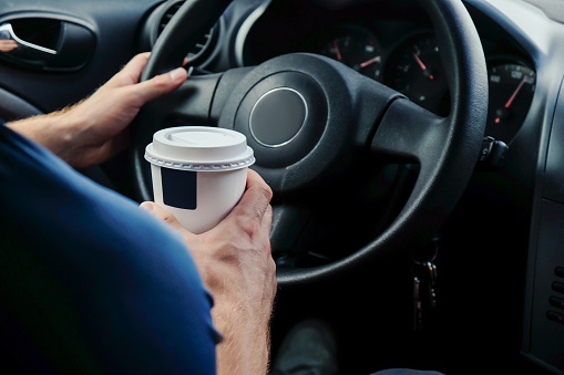 Close up young men holding cup of coffee while driving car