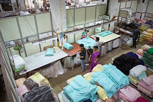 High angle view of male and female workers folding dyed textiles and wrapping them in plastic on floor of Mumbai manufacturing factory.