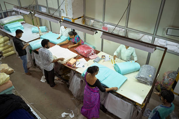 High angle view of male and female Indian workers folding and wrapping textiles in plastic on floor of Mumbai dyeing and printing mill.