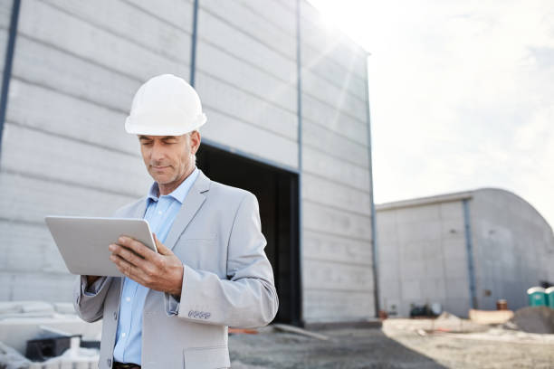 ingénieur mature utilisant sa tablette numérique sur un chantier de construction - building contractor flash photos et images de collection