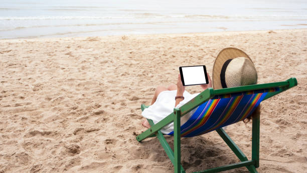 istock a woman holding a black tablet pc with blank desktop screen while lying down on a beach chair 1180347688