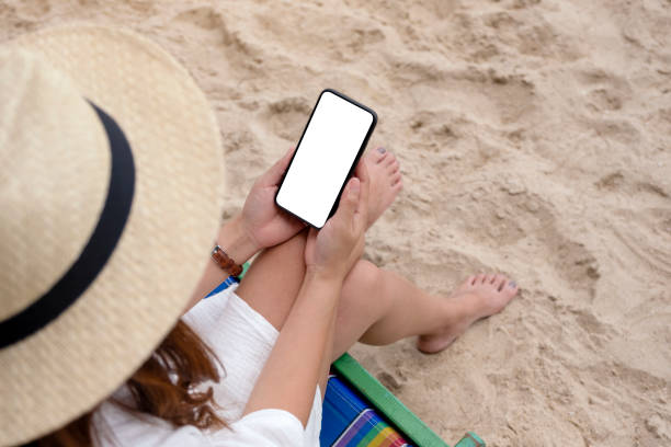 istock a woman holding black mobile phone with blank desktop screen while sitting on a beach chair 1180347756
