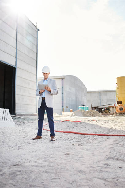 ingénieur mûr restant sur un chantier utilisant sa tablette numérique - building contractor flash photos et images de collection