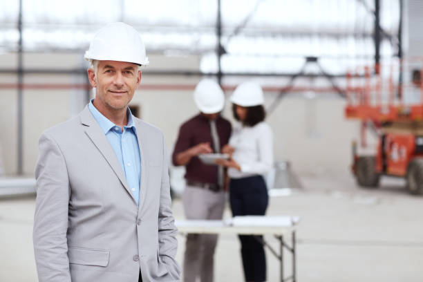 istock Smiling mature building engineer with colleagues working in the background 1180350615