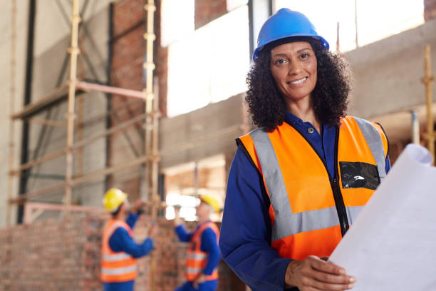 istock Smiling female construction engineer reading blueprints on a building site 1180351447