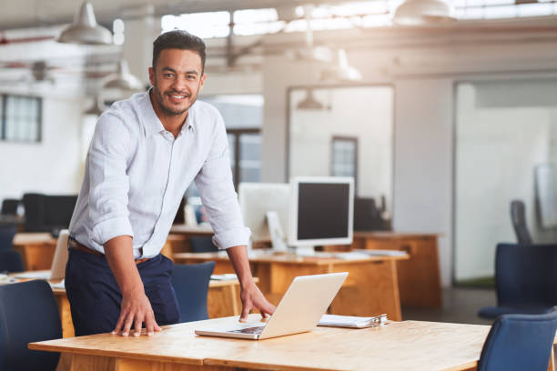 istock Smiling young businessman leaning on his desk using a laptop 1180354461