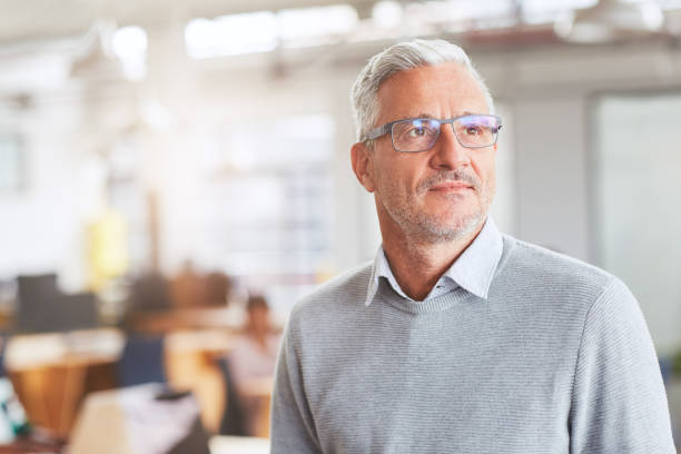 istock Smiling mature businessman standing in an office deep in thought 1180354501