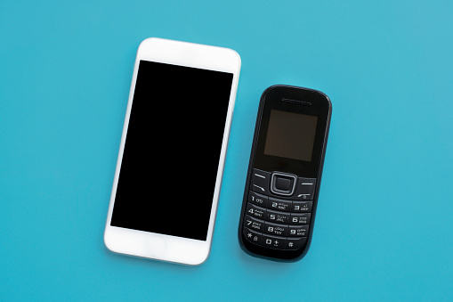 Vintage cell phone with a new generation modern smartphone side by side on blue background