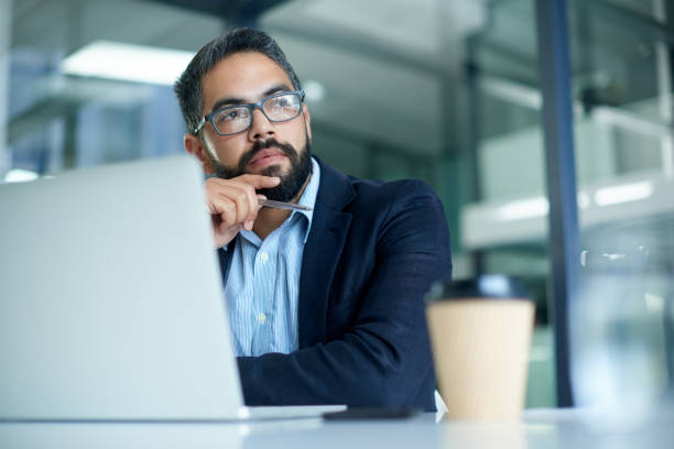 His mind always wanders to success Shot of a mature businessman looking thoughtful while working on a laptop in an office thinks stock pictures, royalty-free photos & images