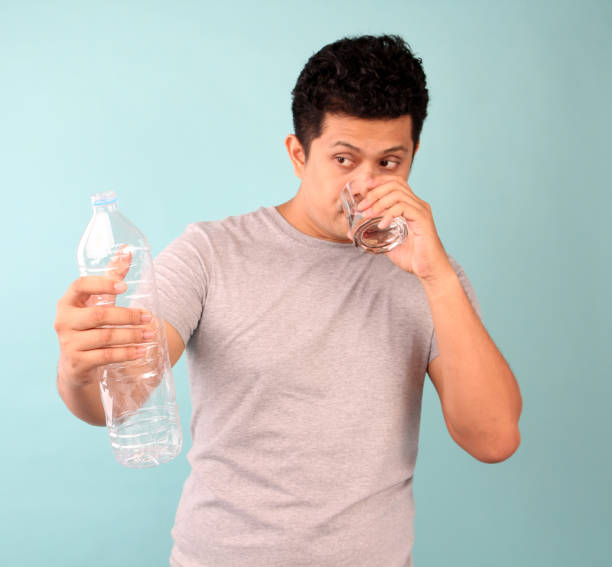 istock A man in a t-shirt on a blue background drinking water from a glass. 1180359183
