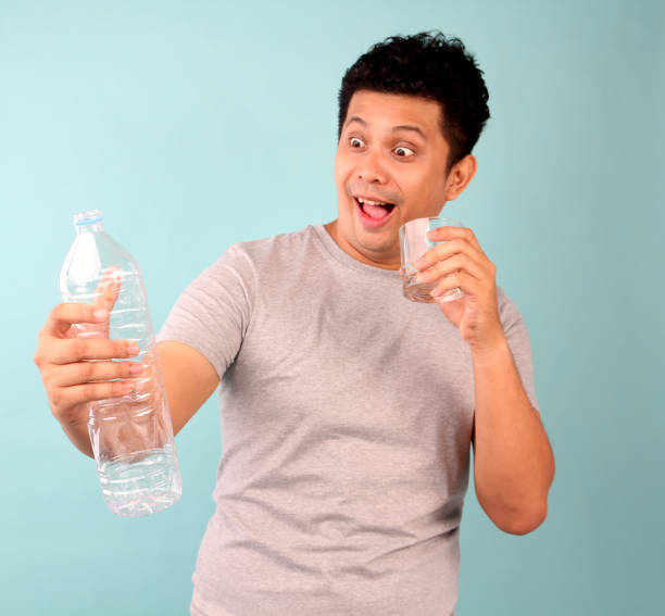 istock A man in a t-shirt on a blue background drinking water from a glass. 1180359193