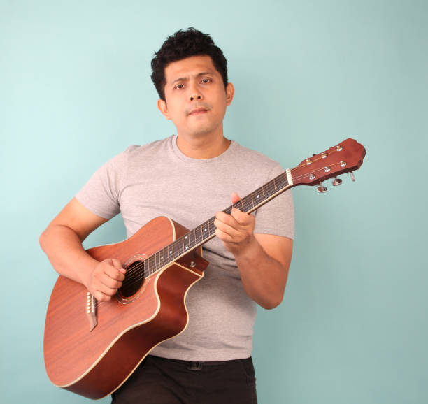 istock Asian man in gray T-shirt playing guitar on a blue background. 1180360352