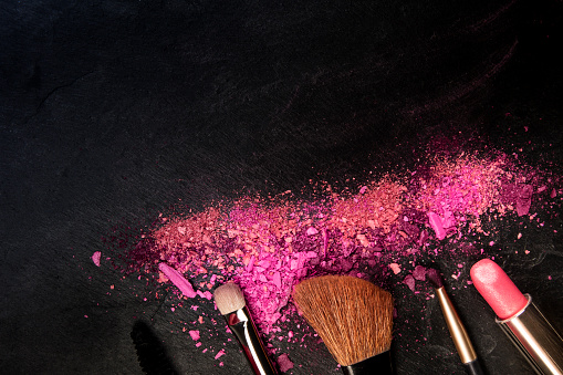 Make-up brushes and lipstick with broken cosmetics, overhead shot on a black background with copy space, a beauty design template for a makeup banner