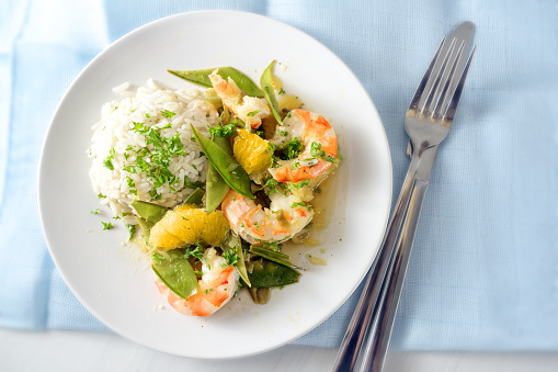 fried tiger prawn shrimp dish with sugar peas, onion, oranges and rice, high angle view from above, copy space, selected focus, narrow depth of field