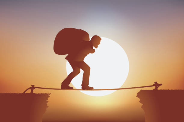 istock A man overcomes an obstacle balanced on a wire carrying a heavy burden on his back. 1180364229