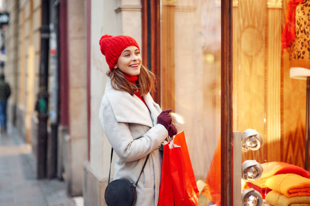 woman looking through the stores window - coat warm clothing one person joy imagens e fotografias de stock