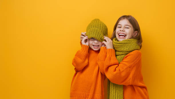 Winter portrait of happy children Winter portrait of happy children wearing knitted hat, snood and sweaters. Girls having fun, playing and laughing on yellow background. Fashion concept. kids winter fashion stock pictures, royalty-free photos & images