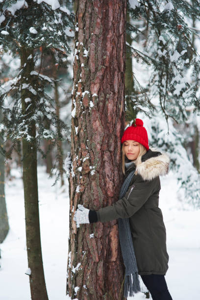 istock Young woman embracing tree in winter forest 1180370186