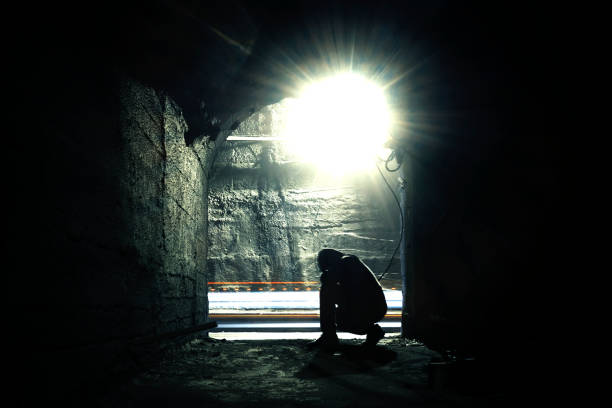 istock A man in a dark underground corridor. Squatting man in an underground corridor 1180370546