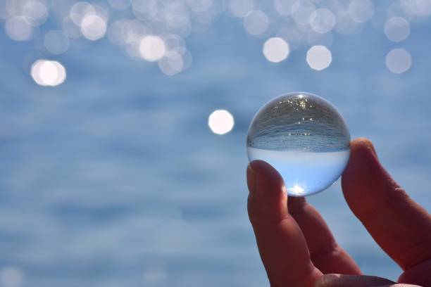 istock Beautiful summer coast seen through a blue glass ball/ Blue freedom concept/ Ocean Surface Ripples and Clouds in Sky Captured in Glass Ball/ Man holding glass ball whit sea reflection 1180372013