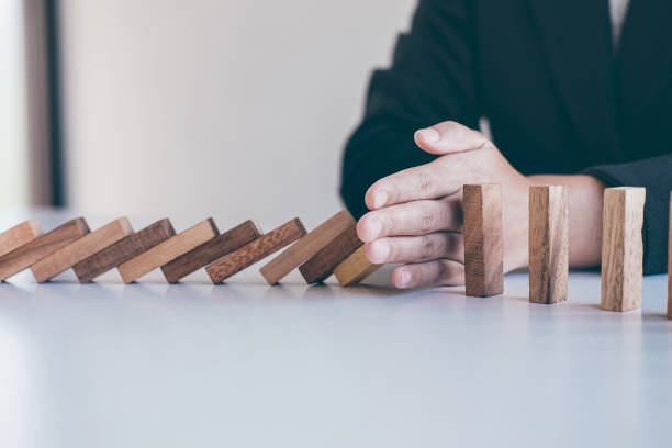 istock Midsection Of Man Stopping Dominos From Falling While Sitting By Table 1180372116