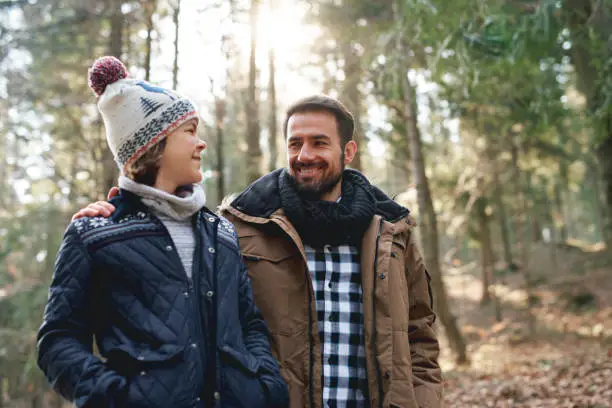 Photo of Happy dad and teenage son walking in the autumn forest