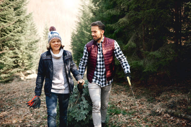 istock Father and son carrying heavy christmas tree 1180378484