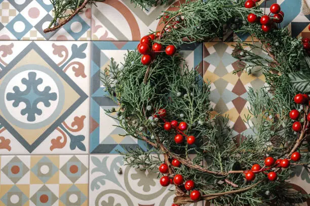 Christmas wreath detail of evergreen, red berries and gold reindeer on retro geometric tiles. Nandian network, green branch and rustic pine crown. Flat lay. Christmas concept. From overhead