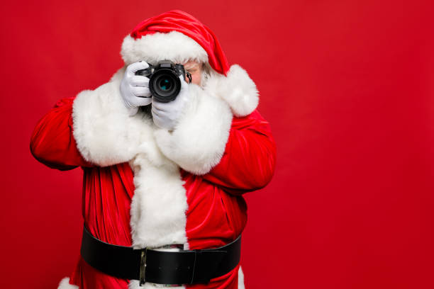 porträt von konzentrierten älteren santa claus hipster fotografieren seine weihnachtsreise ins ausland tragen stilvolle kostüm gürtel handschuhe isoliert über rotem hintergrund - weihnachten fotos stock-fotos und bilder