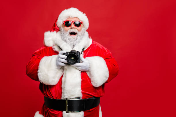 Portrait of excited enthusiastic santa claus in eyewear eyeglasses have voyage take photo wear stylish costume cap hat belt isolated over red background Portrait of excited enthusiastic santa claus in eyewear eyeglasses have voyage take photo, wear stylish costume cap hat belt isolated over red background santa claus photos stock pictures, royalty-free photos & images