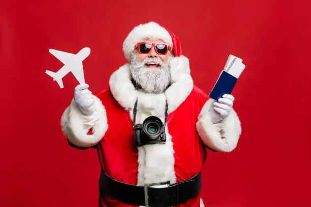 Portrait of funny hipster santa claus have journey abroad in terminal want, travel take photo photographing wear spectacles eyewear eyeglasses costume isolated over red background