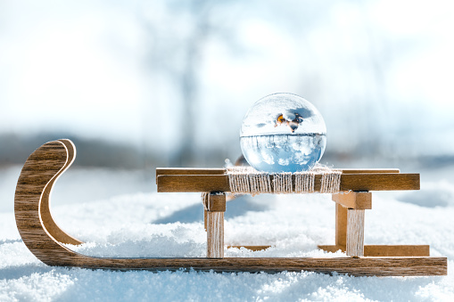 Wooden sledge with a crystal or glass ball, winter landscape reflection with christmas balls, copyspace