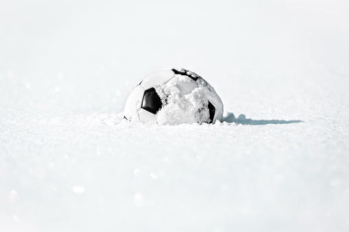 Football or soccer ball in the deep white snow, close season and winter break, copyspace