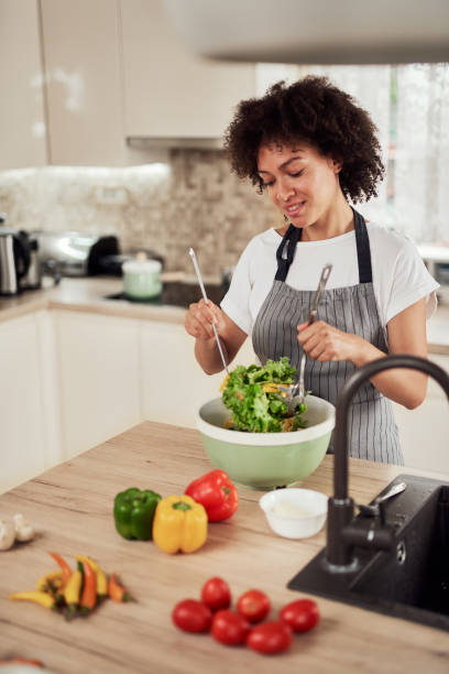 istock Woman mixing vegetables in bowl while standing in kitchen. 1180386502
