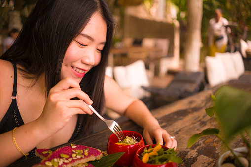 Veggie brunch . natural lifestyle portrait of young happy and beautiful Asian Japanese woman eating outdoors having organic breakfast at cool cafe in vegetarian nutrition and healthy food