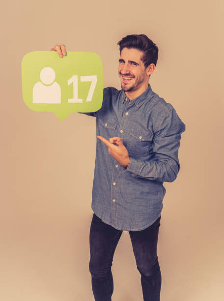 istock Attractive young man holding friend social network notification icon happy to get more friends and followers on the internet or online blog in social media obsession and technology communication. 1180388049