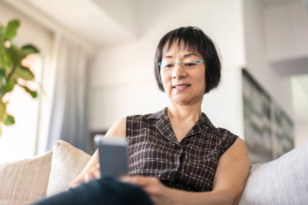 istock Senior Chinese woman using a smartphone on sofa 1180388674